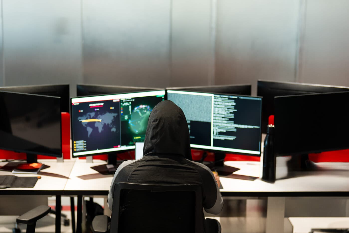 The adversary's side of the screen — hooded operator at red-lit displays